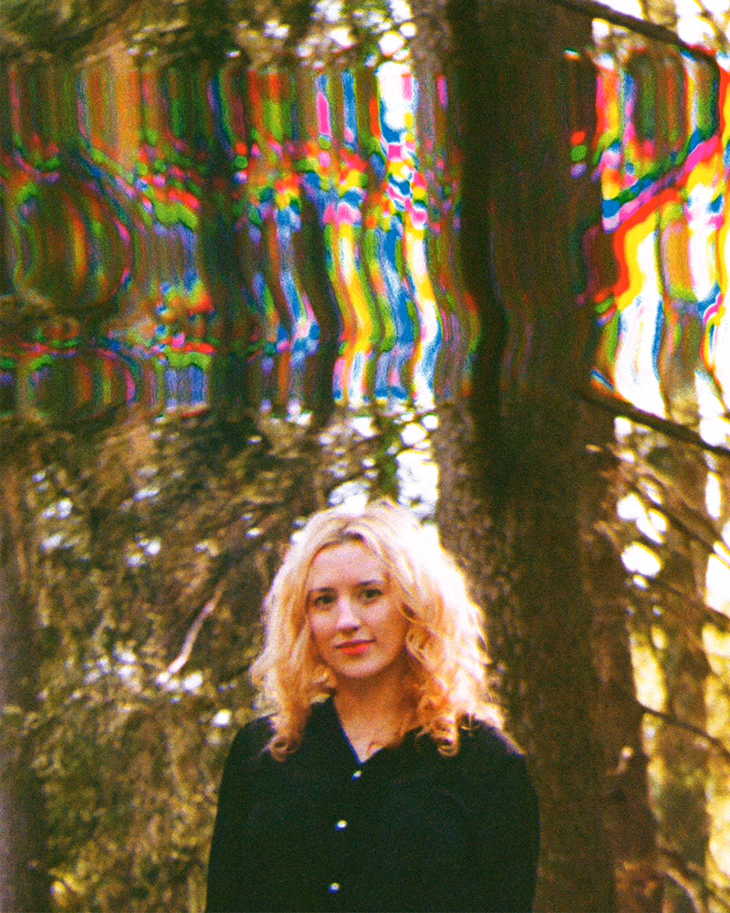 Hannah Telle stands in front of a forest background with a strong colorful glitch effect.